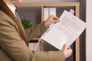 Businesswoman putting document into punched pocket in office, closeup