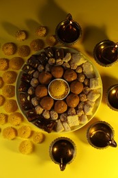 Happy Diwali. Flat lay composition with diya lamps, chrysanthemum flowers and delicious Indian sweets on yellow table