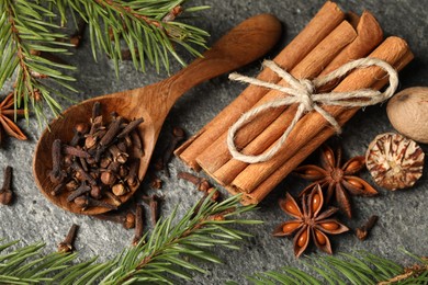 Photo of Wooden spoon with different spices, nuts and fir branches on gray table, flat lay