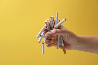 Photo of Stop smoking. Woman holding whole and broken cigarettes on yellow background, closeup. Space for text