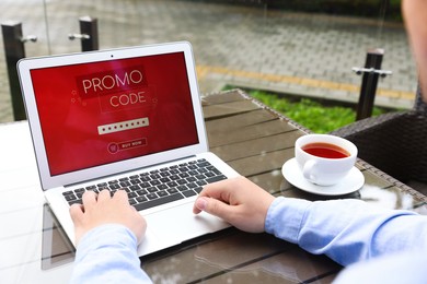 Photo of Man with laptop activating promo code at wooden table outdoors, closeup