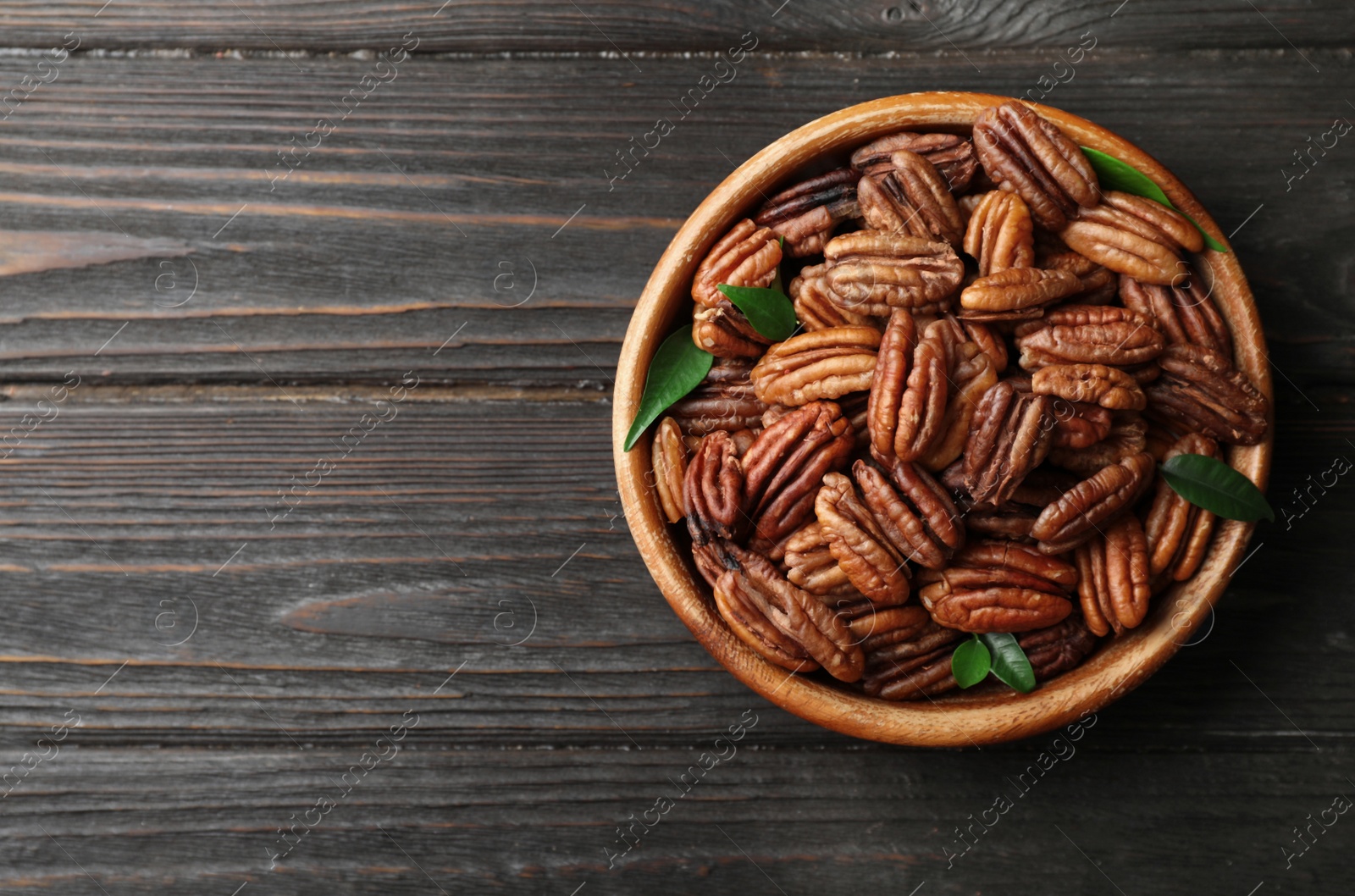 Photo of Dish with shelled pecan nuts on wooden background, top view. Space for text