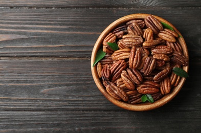 Photo of Dish with shelled pecan nuts on wooden background, top view. Space for text