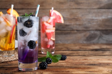 Photo of Delicious blackberry lemonade made with soda water and fresh ingredients on wooden table. Space for text