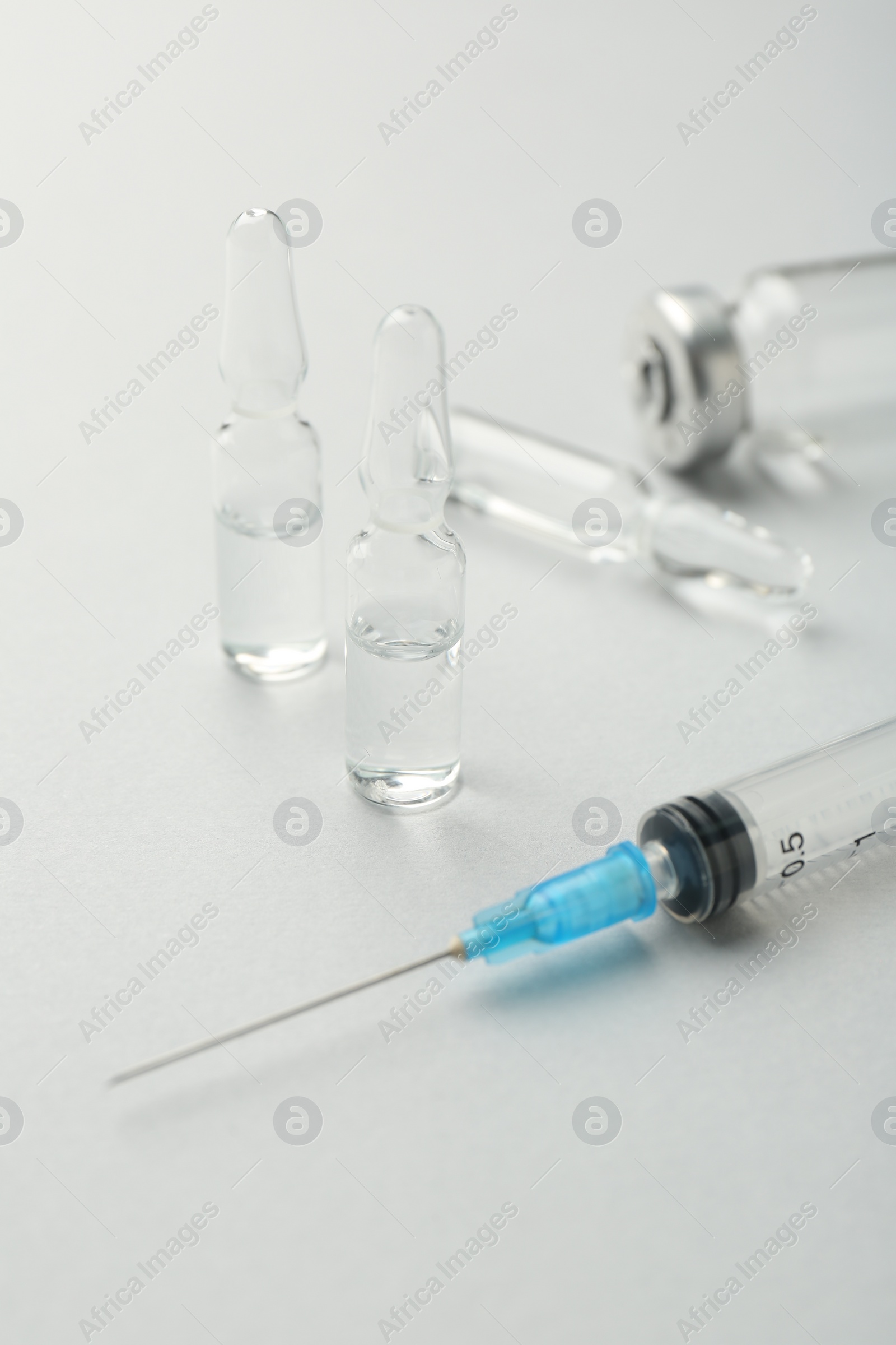 Photo of Glass ampoules with liquid and syringe on white background, closeup