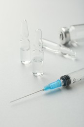 Photo of Glass ampoules with liquid and syringe on white background, closeup