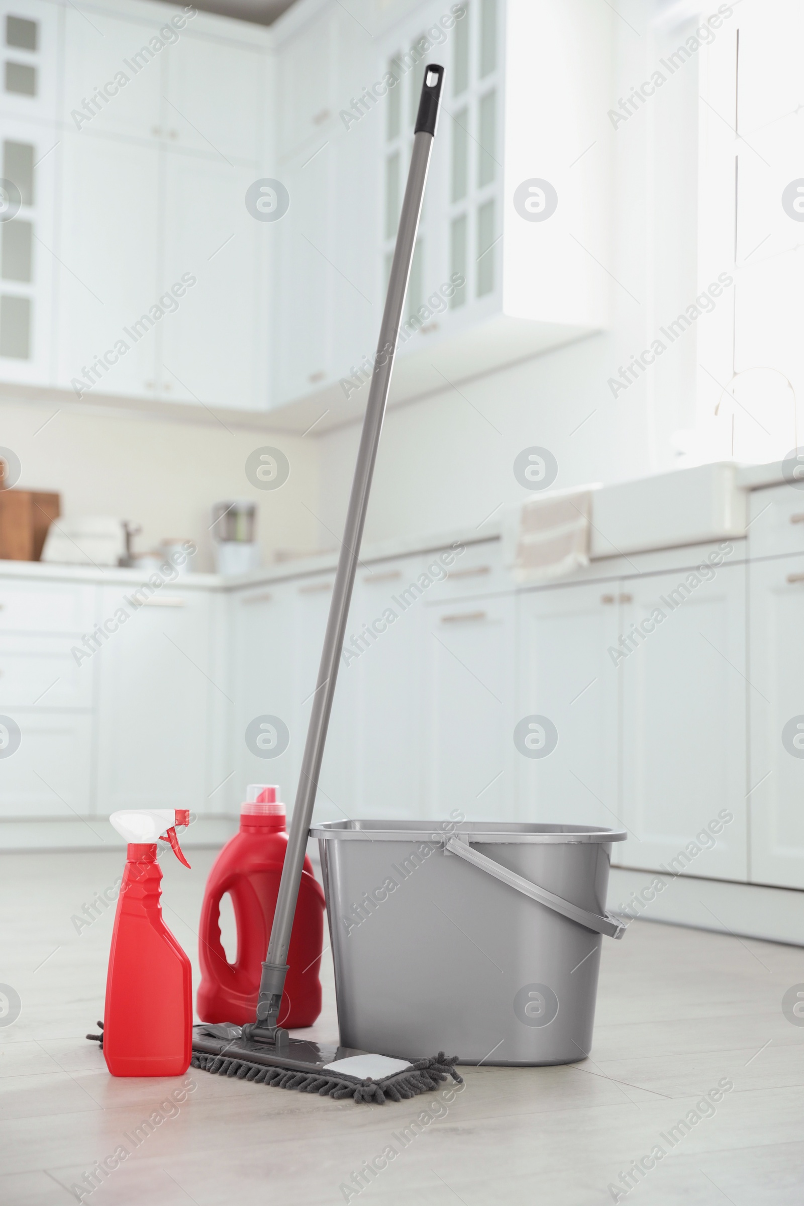 Photo of Mop, detergents and plastic bucket in kitchen. Cleaning supplies