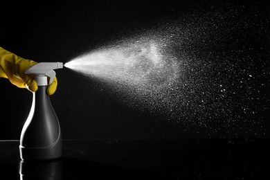 Photo of Woman spraying liquid from bottle on black background, closeup