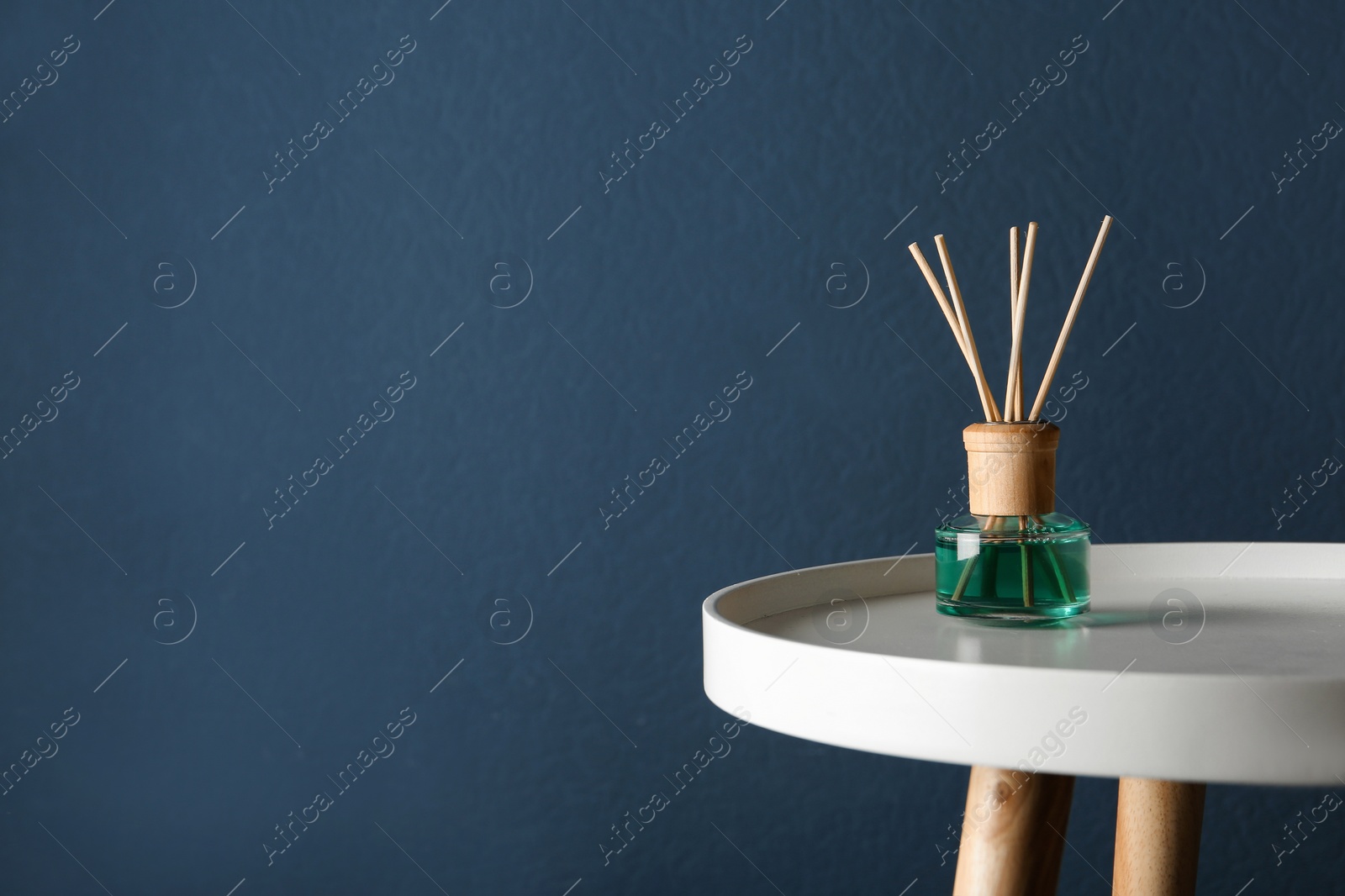 Photo of Reed air freshener on table against dark blue background, space for text