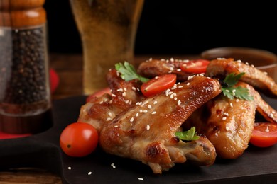 Glass of beer and delicious baked chicken wings with ingredients on wooden table, closeup