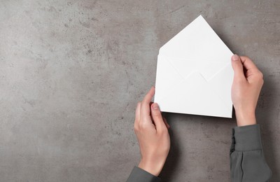 Woman with letter envelope at grey textured table, top view. Space for text