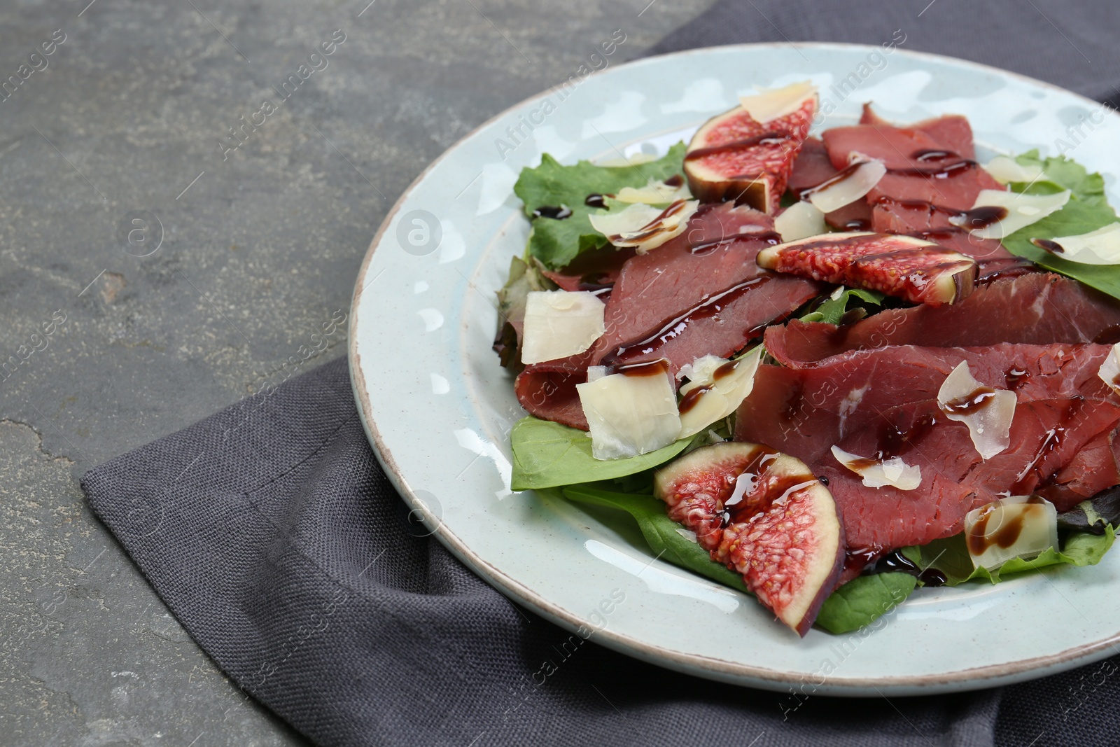 Photo of Plate with delicious bresaola salad on grey textured table, closeup. Space for text