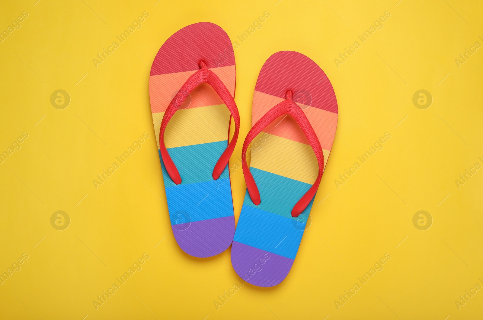 Photo of Rainbow flip flops on yellow background, flat lay. LGBT pride