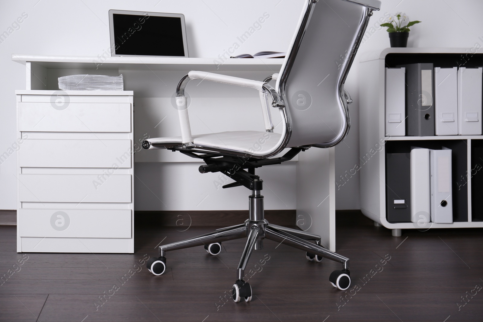 Photo of Comfortable rolling chair near table with laptop in modern office