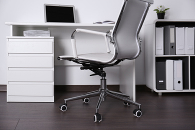 Photo of Comfortable rolling chair near table with laptop in modern office