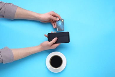 Online payment. Man with smartphone, credit card and coffee on light blue background, top view