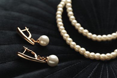 Photo of Elegant necklace and golden earrings with pearls on black fabric, closeup