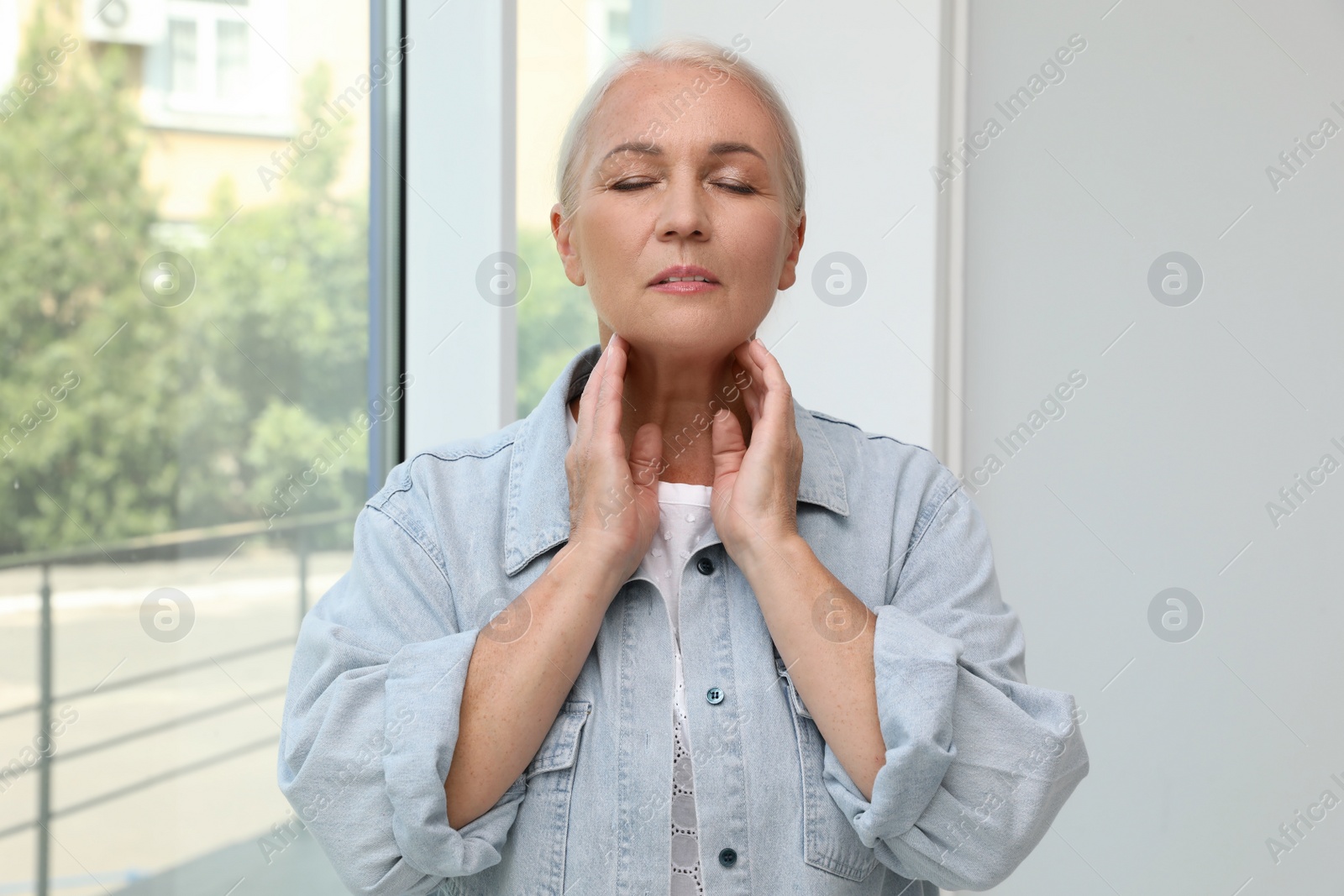 Photo of Mature woman doing thyroid self examination near window