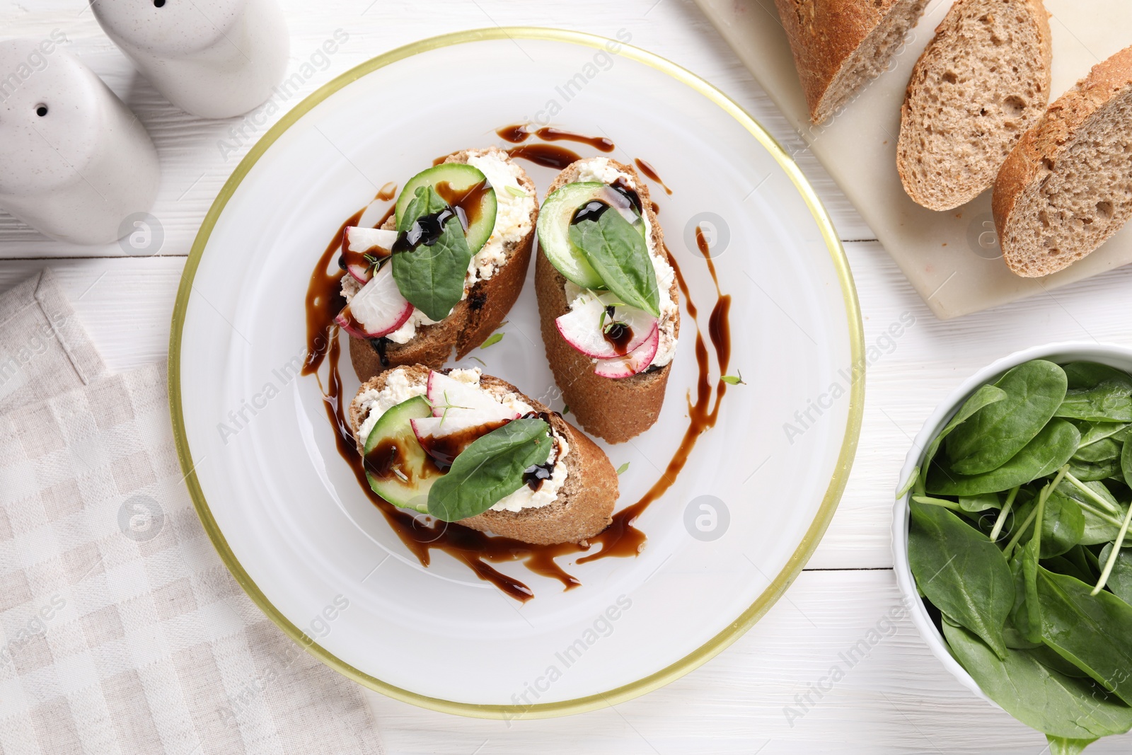 Photo of Delicious bruschettas with cream cheese, vegetables, balsamic vinegar and ingredients on white wooden table, flat lay