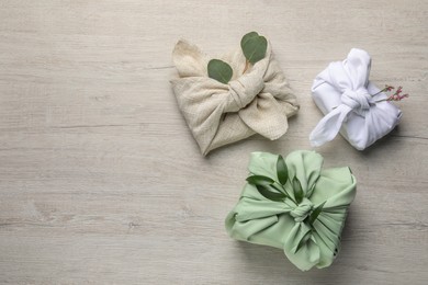 Photo of Furoshiki technique. Gifts packed in different fabrics and decorated with plants on wooden table, flat lay with space for text
