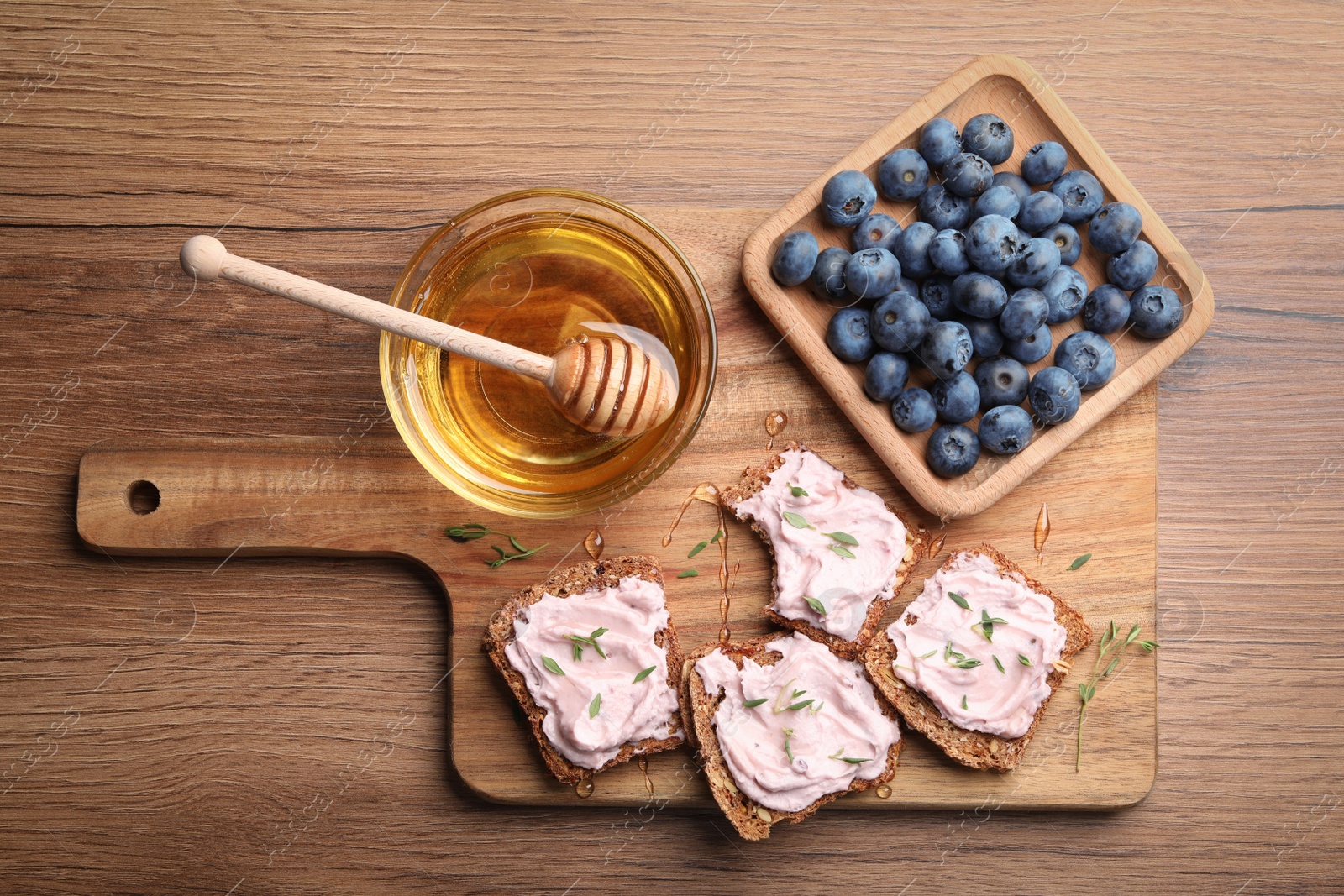 Photo of Tasty sandwiches with cream cheese, honey and thyme on wooden table, flat lay