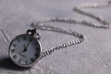 Silver pocket clock with chain on grey textured table, closeup. Space for text
