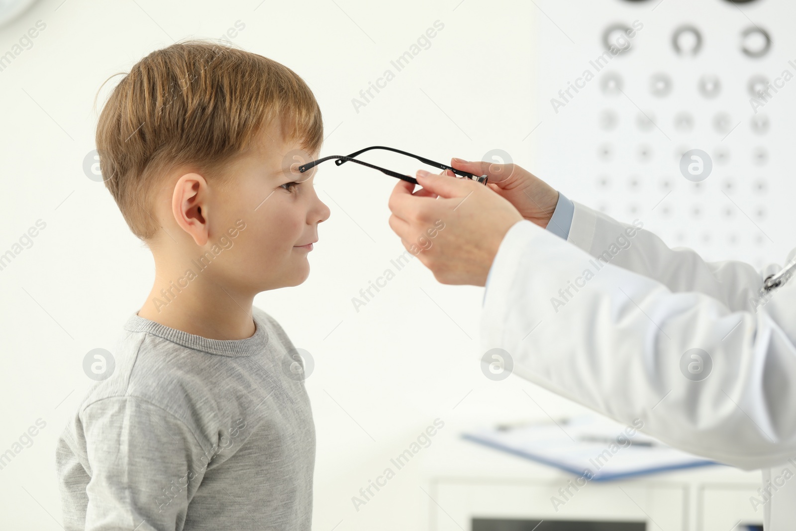 Photo of Vision testing. Ophthalmologist giving glasses to little boy indoors