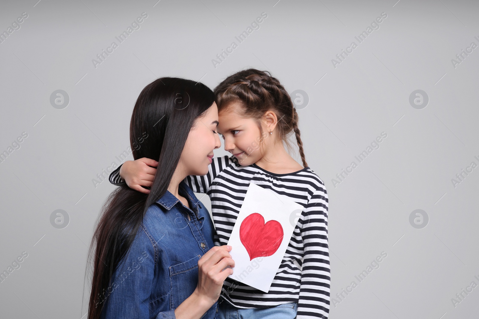 Photo of Happy woman with her daughter and handmade greeting card on light grey background. Mother's day celebration