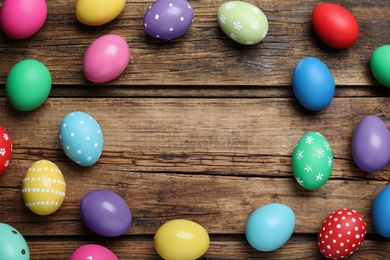 Frame of colorful eggs on wooden background, flat lay with space for text. Happy Easter