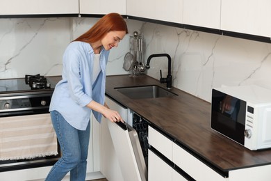 Photo of Smiling woman pushing button on dishwasher's door in kitchen