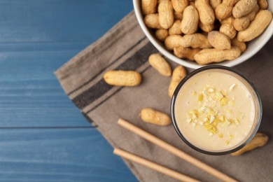 Photo of Glass of tasty banana smoothie with peanuts on light blue wooden table, flat lay. Space for text