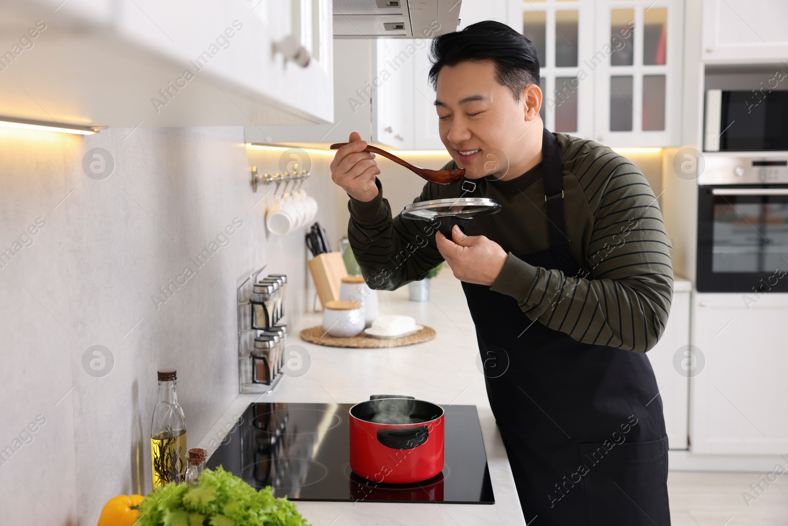 Photo of Cooking process. Man tasting dish in kitchen