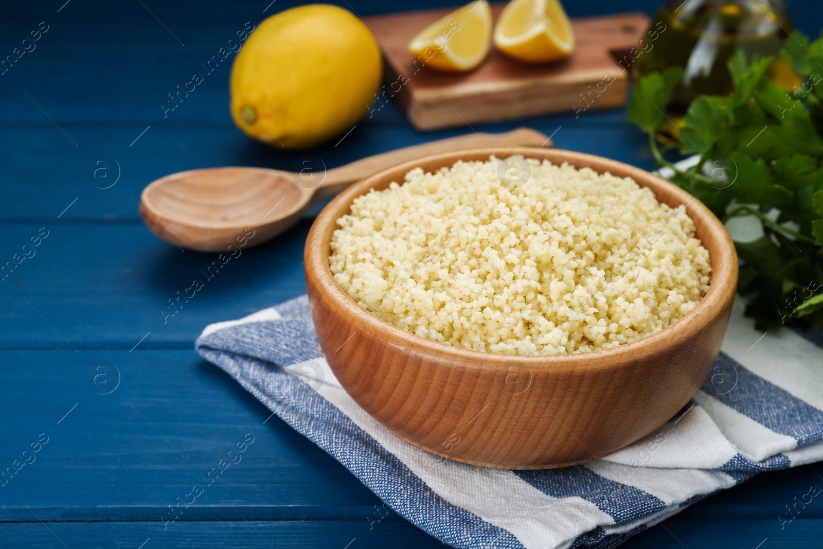 Photo of Bowl of tasty couscous on blue wooden table, closeup. Space for text