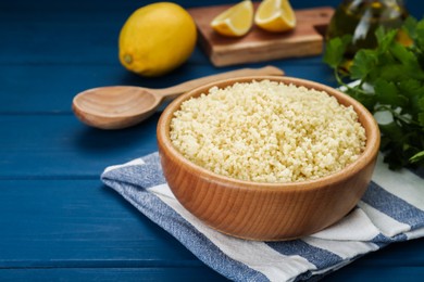 Bowl of tasty couscous on blue wooden table, closeup. Space for text