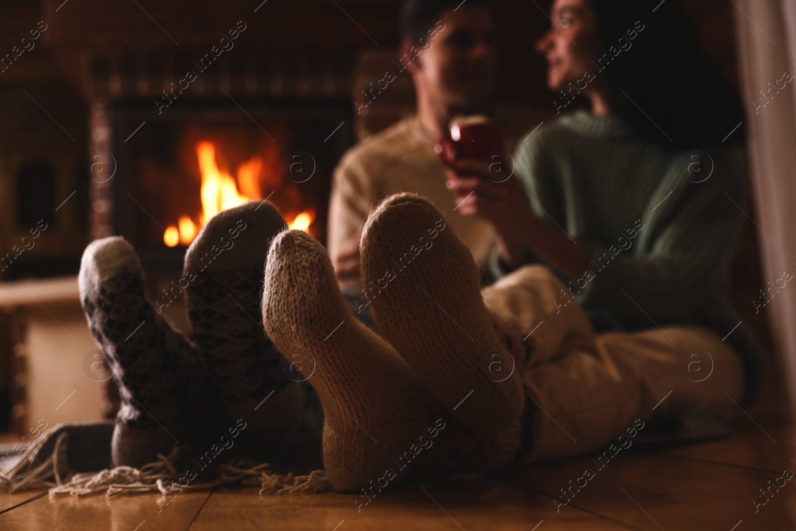 Photo of Lovely couple with delicious cocoa near fireplace at home, focus on feet. Winter vacation