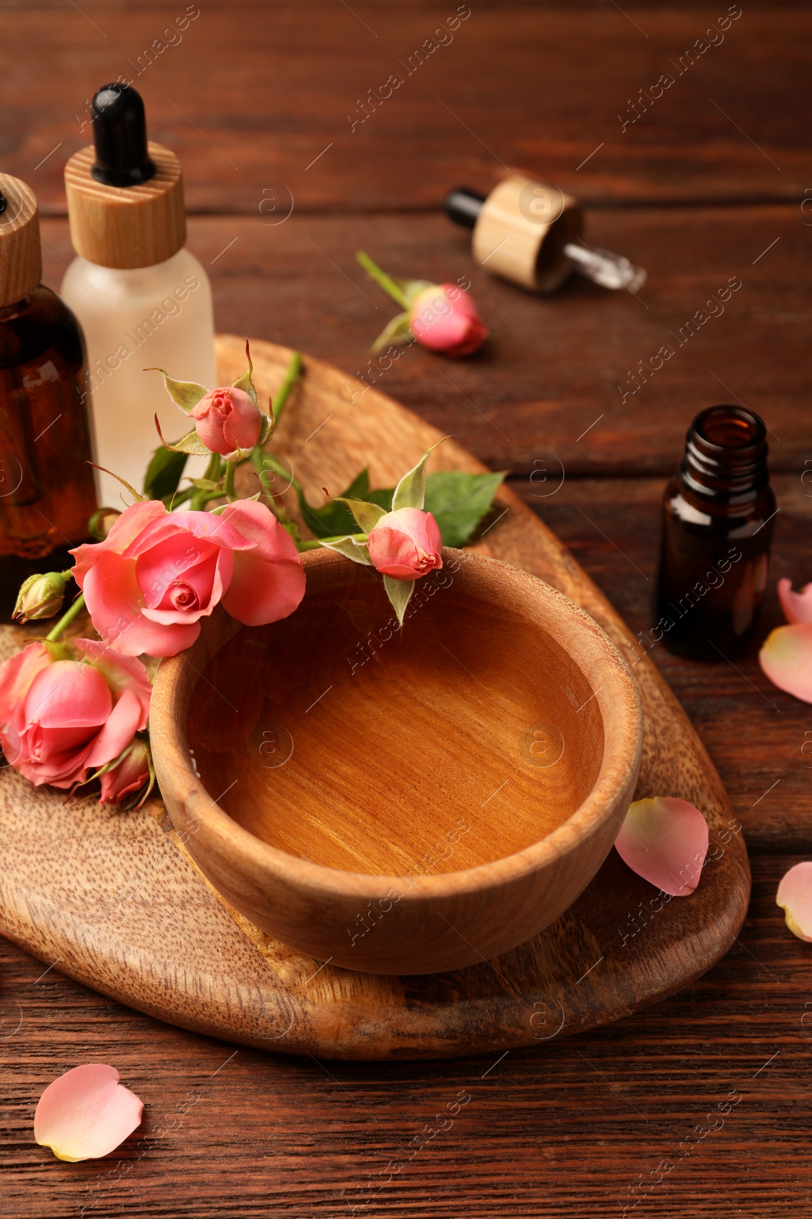 Photo of Bowl of essential oil and beautiful roses on wooden table. Aromatherapy treatment