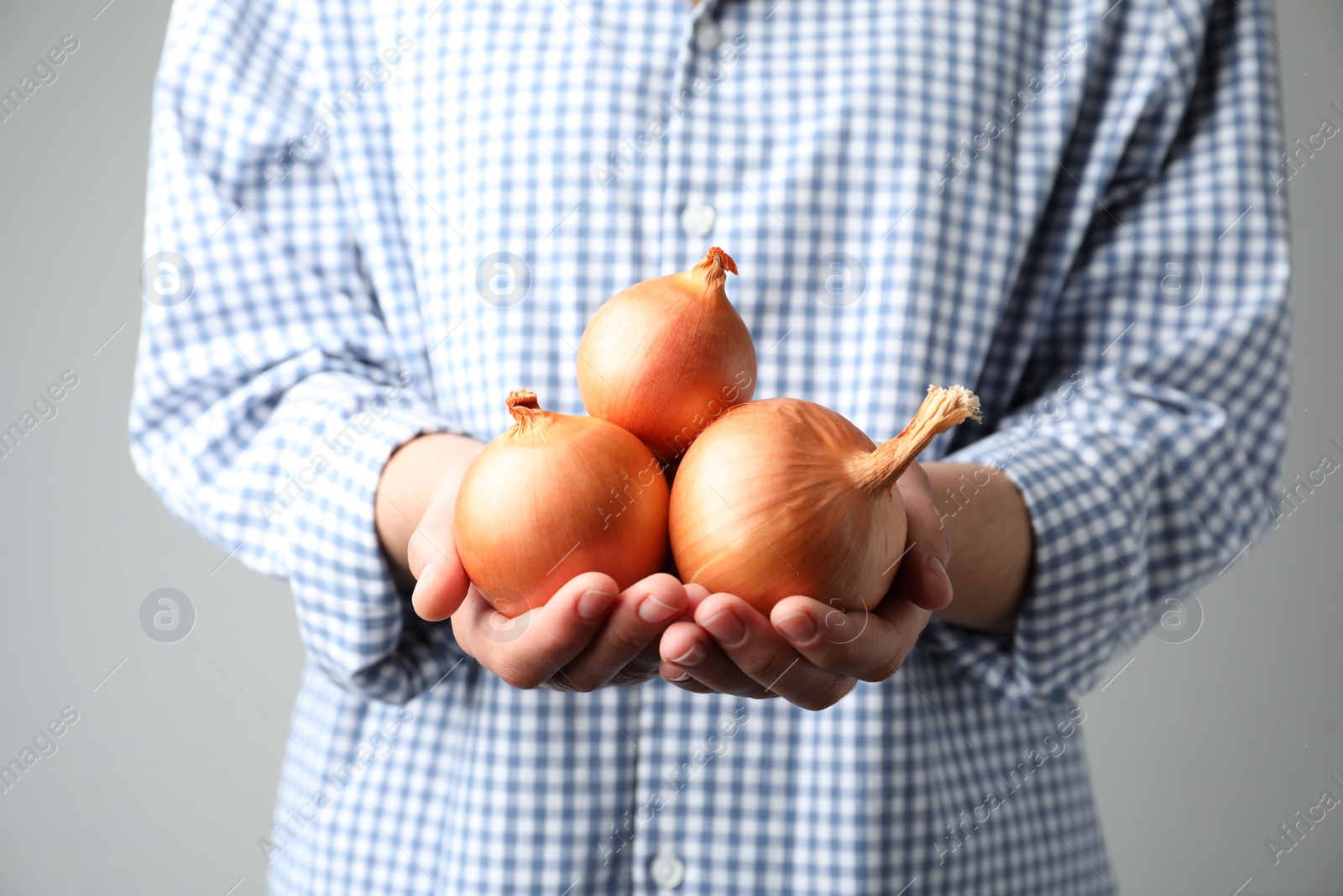 Photo of Woman holding raw yellow onion bulbs on grey background, closeup