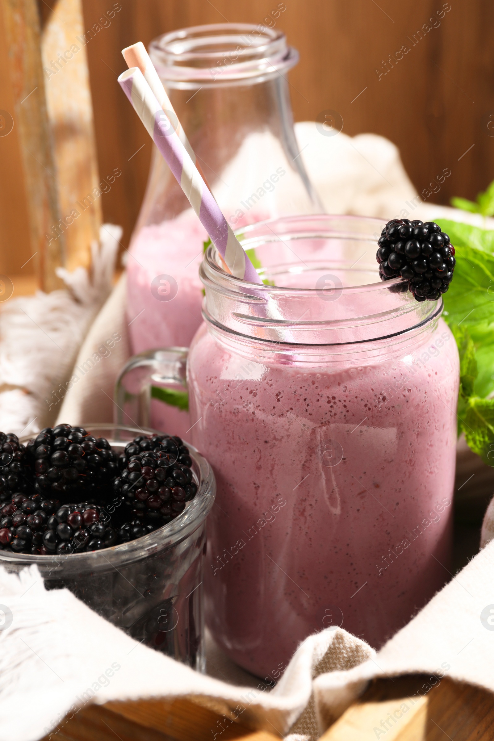 Photo of Different glassware of delicious blackberry smoothie and fresh berries on wooden background, closeup