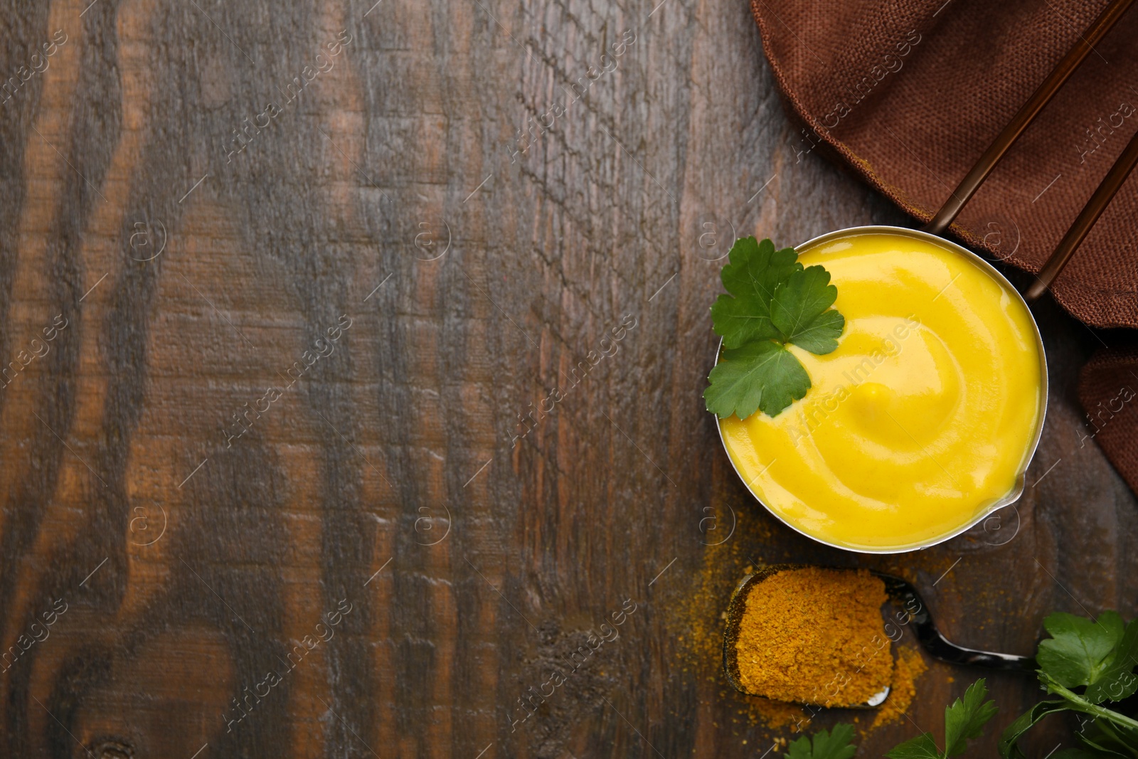 Photo of Saucepan with tasty curry sauce, powder and parsley on wooden table, flat lay. Space for text