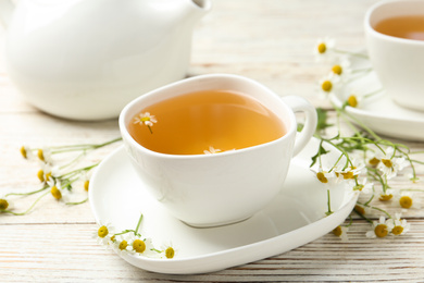 Photo of Cup of tea and chamomile flowers on white wooden table