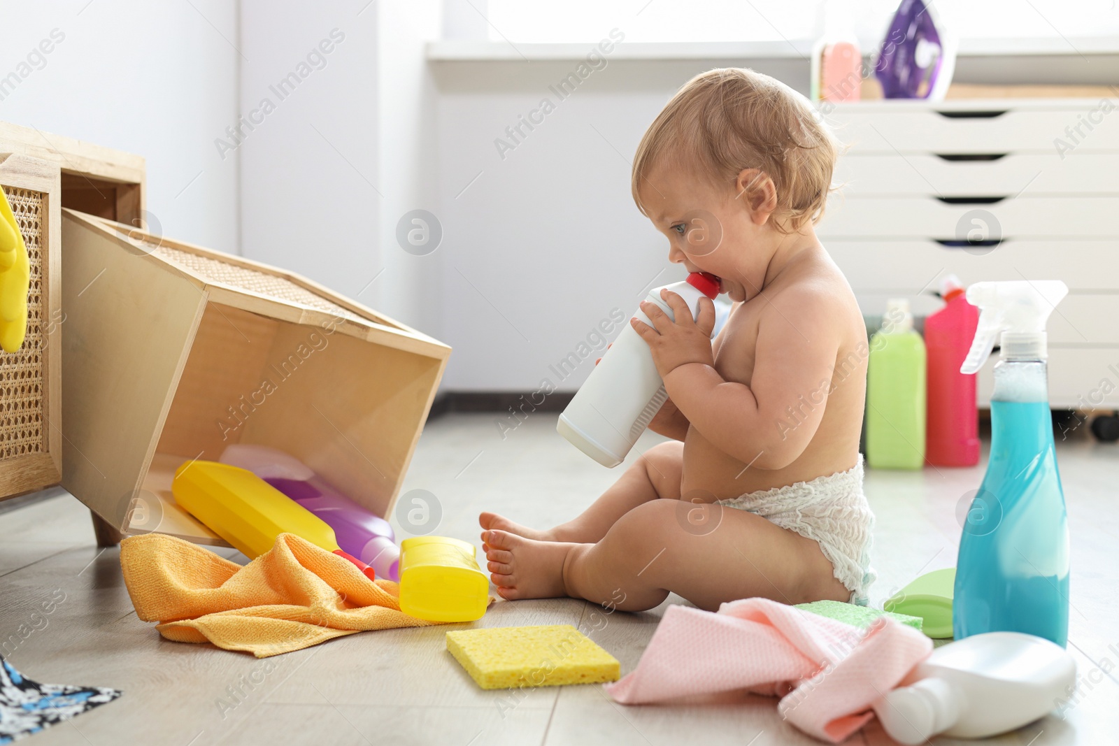 Photo of Cute baby playing with bottle of detergent on floor at home. Dangerous situation