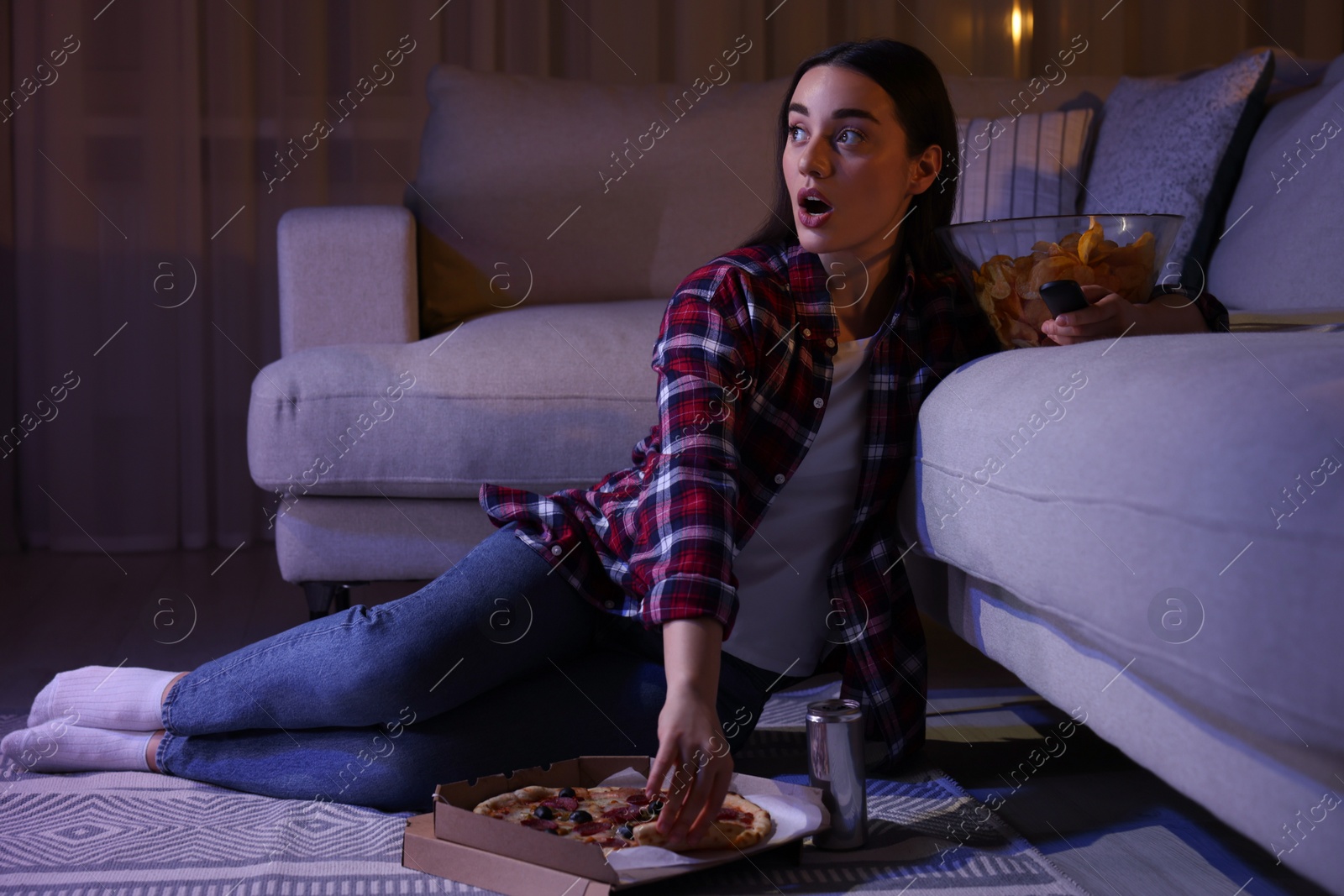 Photo of Young woman eating pizza while watching TV in room at night. Bad habit