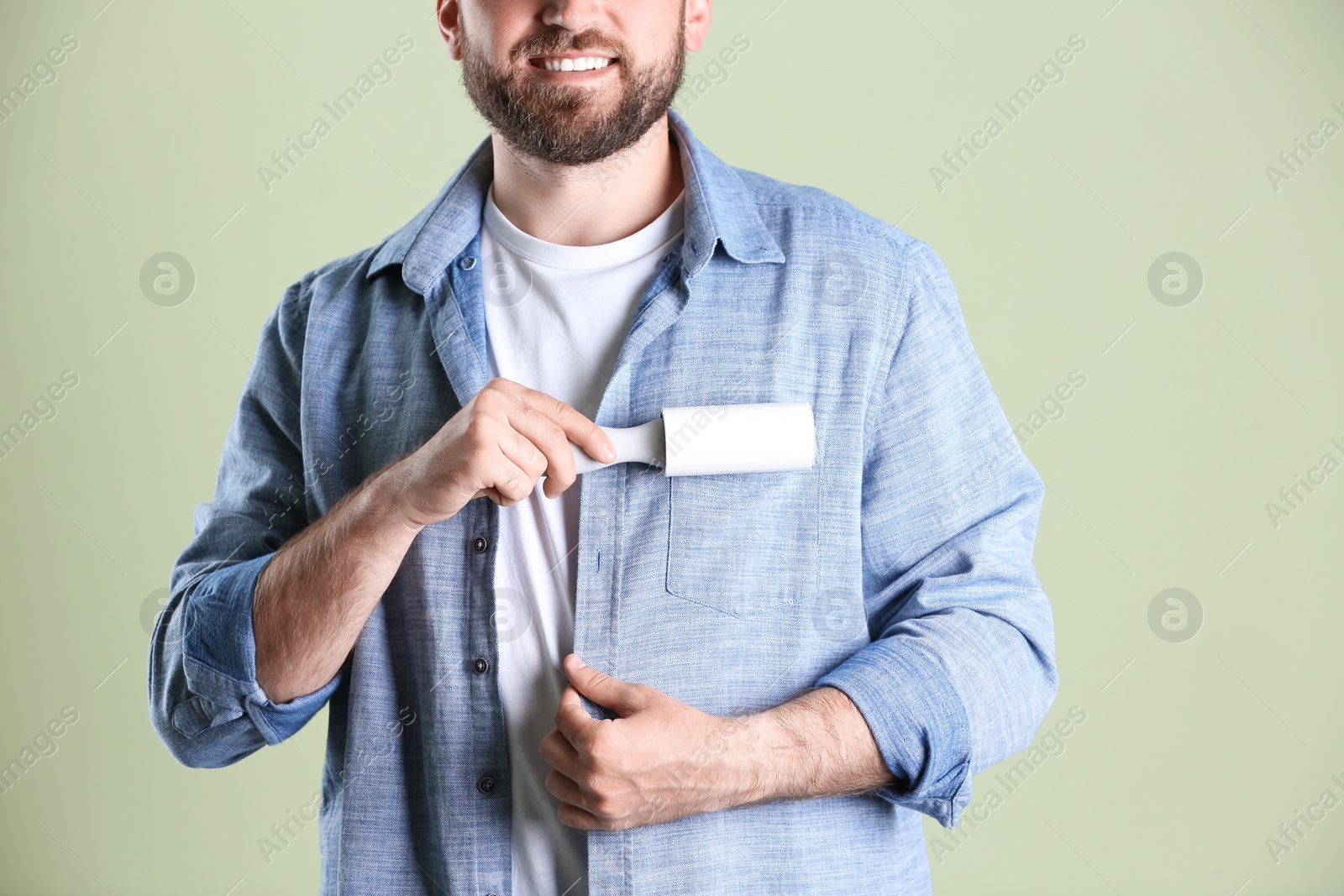 Photo of Man cleaning clothes with lint roller on light background, closeup