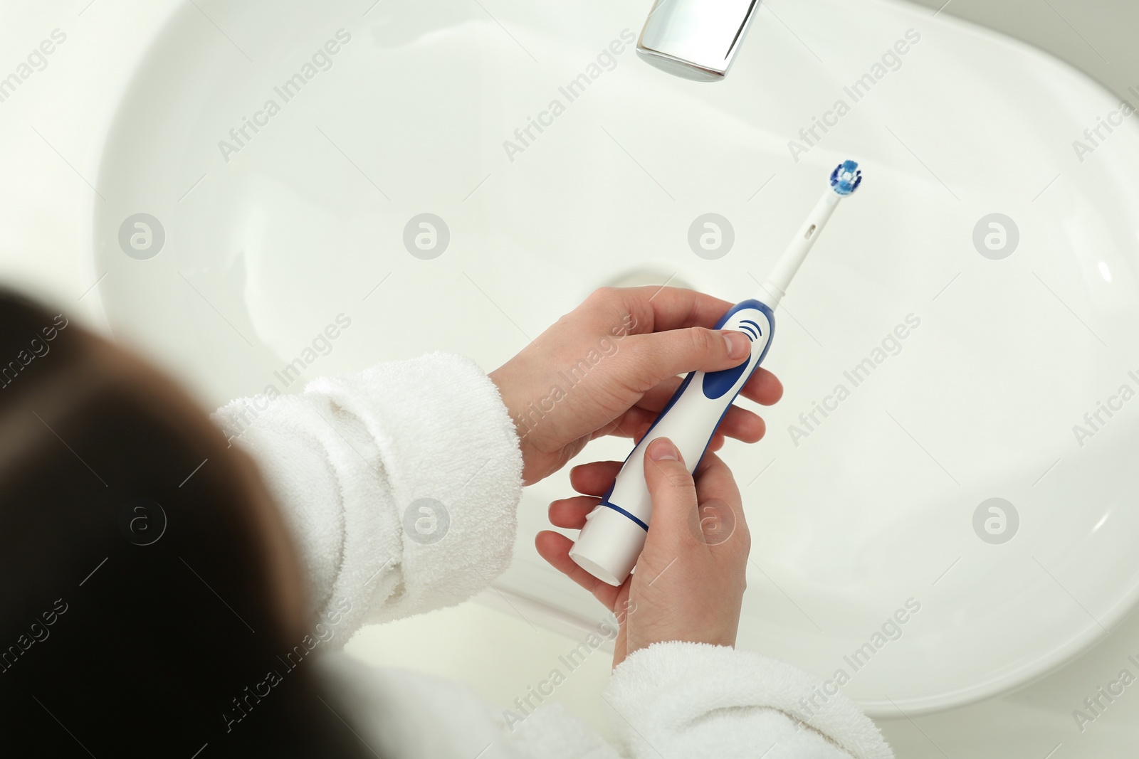 Photo of Woman turning on electric toothbrush above sink in bathroom, closeup