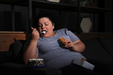 Photo of Depressed overweight woman eating sweets in living room at night