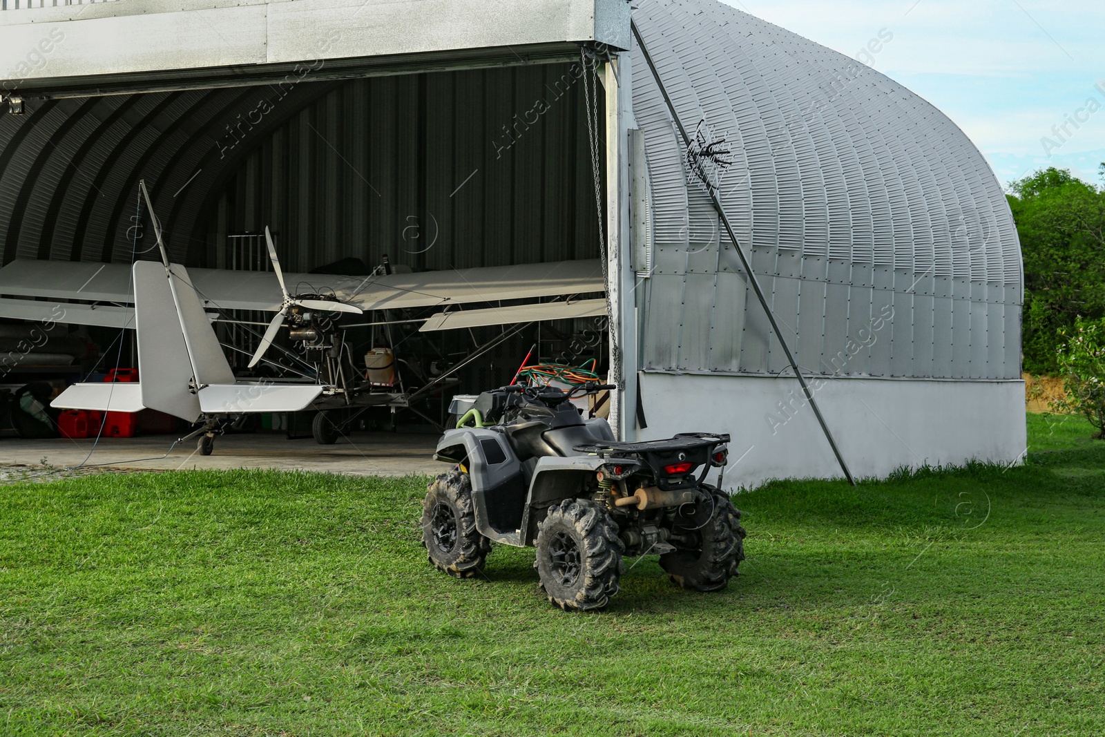 Photo of Modern white airplane in big hangar and quad bike on green grass outdoors