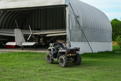 Photo of Modern white airplane in big hangar and quad bike on green grass outdoors