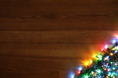 Colorful Christmas lights on wooden table, top view. Space for text