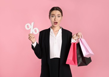 Photo of Surprised young woman with shopping bags and percent symbol figure on light pink background. Big sale