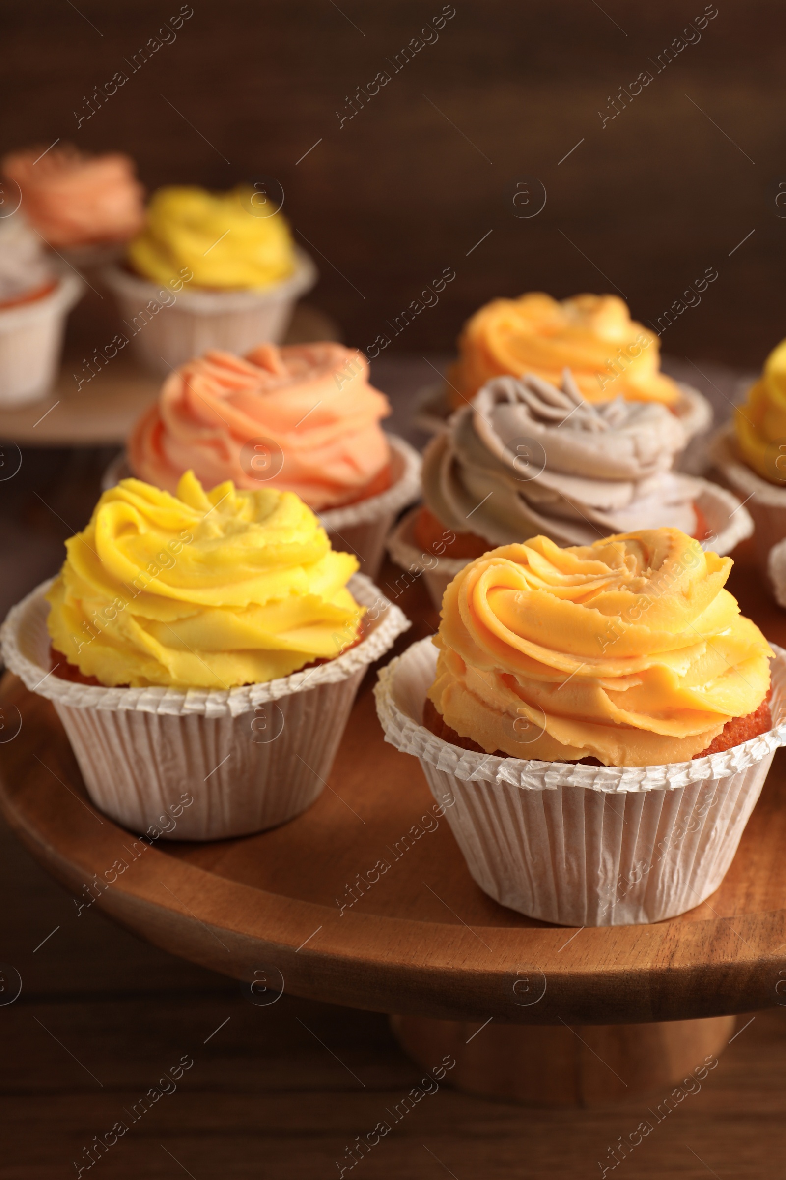 Photo of Tasty cupcakes with cream on wooden stand, closeup